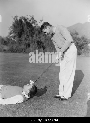 Man hitting golf ball on mans forehead Stock Photo