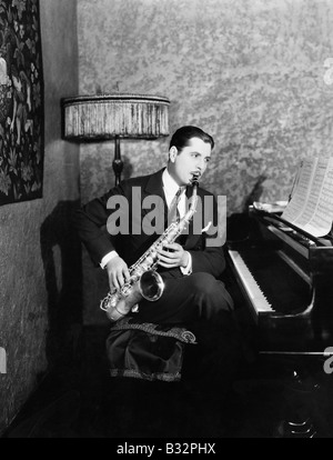 Man sitting at piano playing saxophone Stock Photo