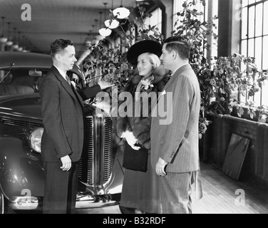 Man and woman standing in a car showroom talking to a salesman Stock Photo