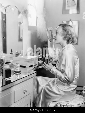 Woman sitting in front of her vanity putting perfume on her eyebrows Stock Photo