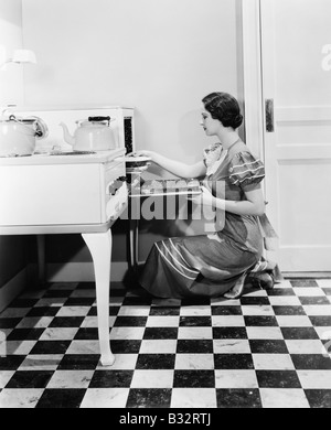 Profile of a young woman putting a pie into an oven Stock Photo