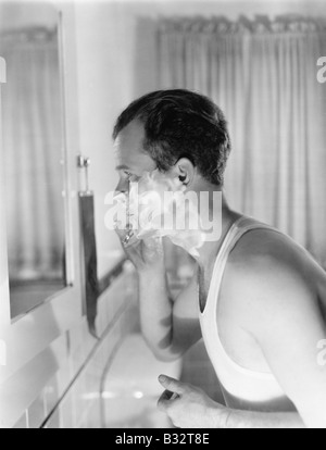 Profile of a young man in front of a mirror  in a bathroom shaving Stock Photo
