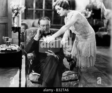 Profile of a young woman showing a book to a man sitting in an armchair Stock Photo