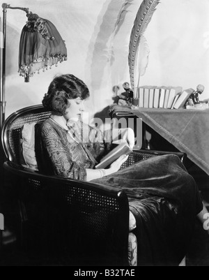 Profile of a young woman sitting in an armchair and reading a book Stock Photo