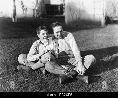 Father and son sitting together on the grass in the back yard Stock Photo