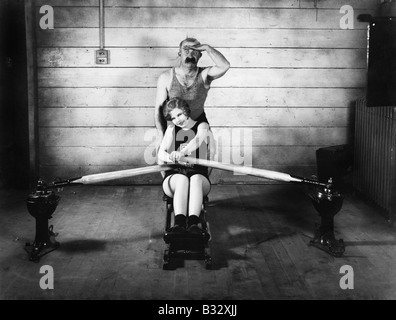 Woman sitting on a rowing machine with a man behind her Stock Photo