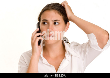 A young woman scratches her head and bites her lip when a phone call confuses her Stock Photo