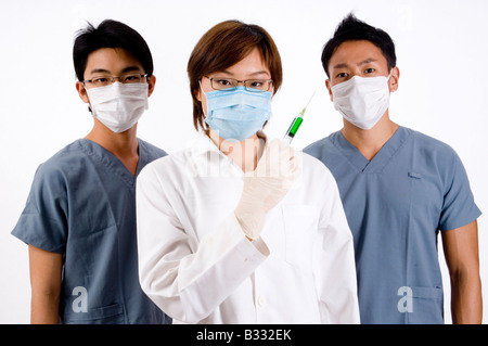 A young female doctor holds a green syringe partnered by two male doctors Stock Photo