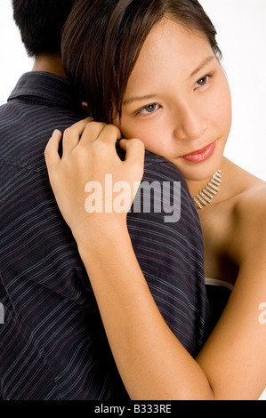 A pretty young asian woman rests her head on a man's shoulders and gazes into the distance Stock Photo