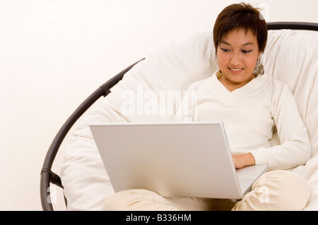A pretty young asian teenager surfs the internet in a big comfy chair Stock Photo