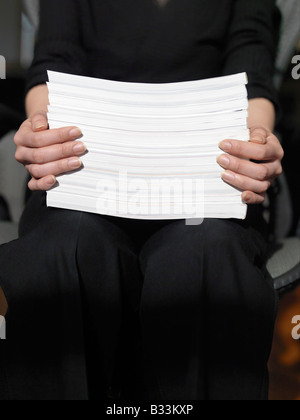 A close up view of female hands holding up a stack of paper while sitting Stock Photo