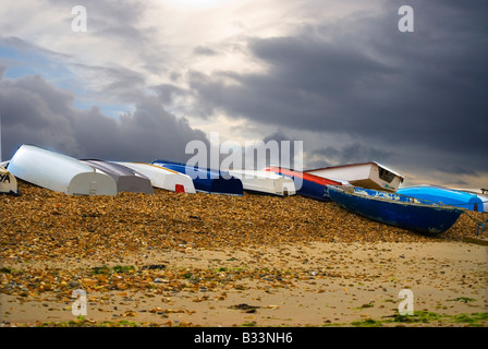 Colourful GRP and wooden dinghys and tenders on a shingle foreshore with a backdrop of stormy clouds. Stock Photo