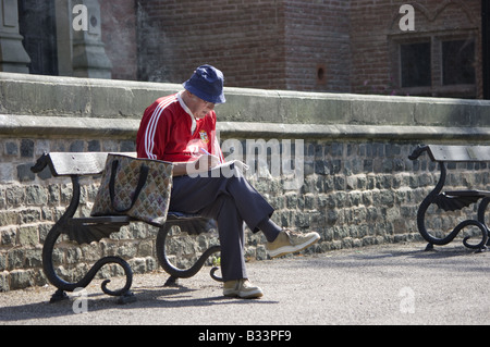 Old man sat on a bench in a park doing a crossword Stock Photo