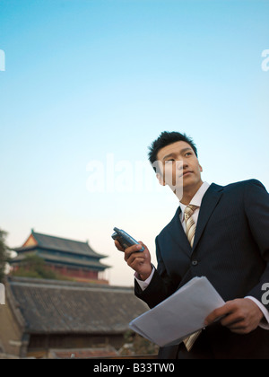 Chinese Businessman reviewing some documents and using his mobile phone for business purposes. Stock Photo