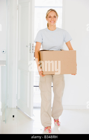 Woman with box moving into new home smiling Stock Photo