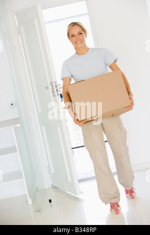 Woman with box moving into new home smiling Stock Photo