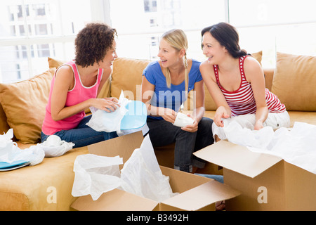 Three girl friends unpacking boxes in new home smiling Stock Photo