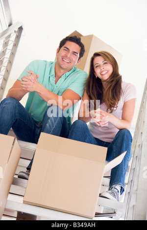 Couple sitting on staircase with boxes in new home smiling Stock Photo