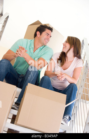 Couple sitting on staircase with boxes in new home smiling Stock Photo