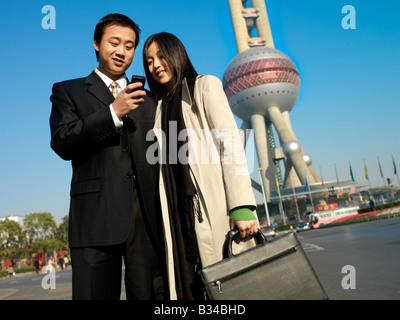 Chinese couple standing before the Pearl Tower in Shanghai China using their phones to communicate with people. Stock Photo