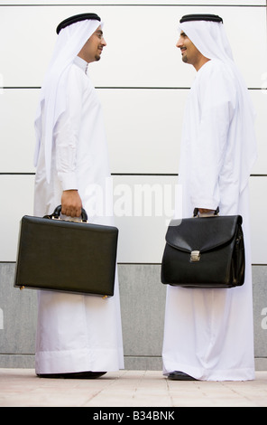 Two businessmen standing outdoors with briefcases smiling Stock Photo