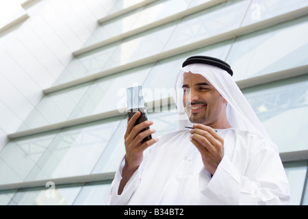Businessman standing outdoors by building using personal digital assistant and smiling (selective focus) Stock Photo