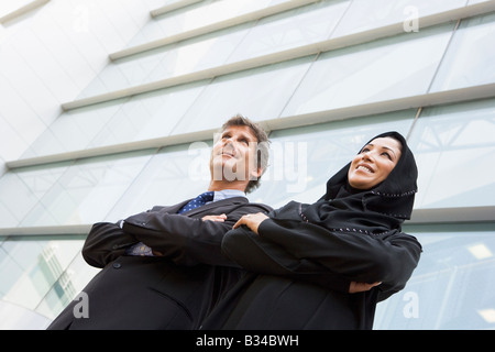 Two businesspeople standing outdoors by building smiling (selective focus) Stock Photo
