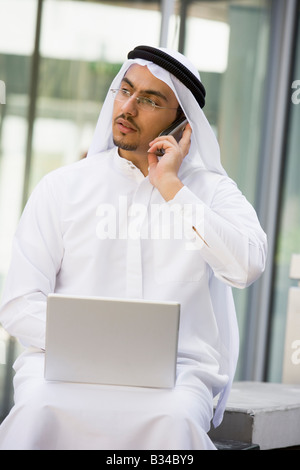 Businessman outdoors with laptop using cellular phone by building (selective focus) Stock Photo