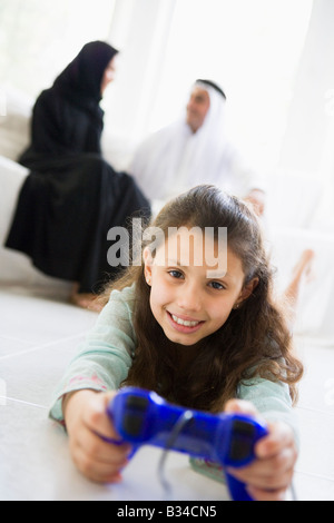 Daughter in living room playing video games smiling with parents in background (high key/selective focus) Stock Photo