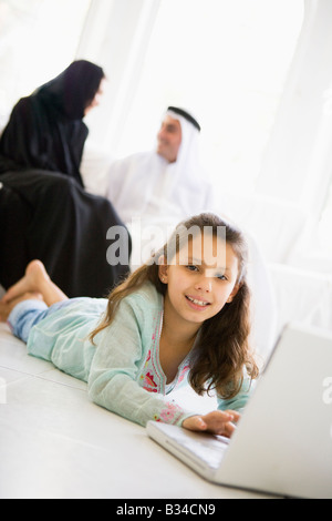 Daughter in living room using laptop and smiling with parents in background (high key/selective focus) Stock Photo
