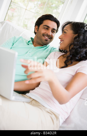 Couple in living room with laptop smiling (high key/selective focus) Stock Photo
