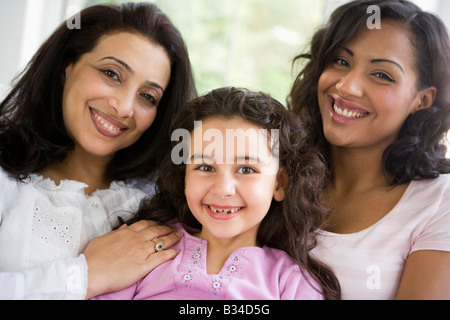 Two women and young girl in living room embracing and smiling (high key) Stock Photo