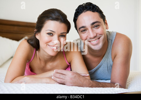 Couple relaxing on bed in bedroom smiling (selective focus) Stock Photo