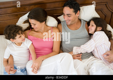 Family relaxing on bed in bedroom smiling (selective focus) Stock Photo