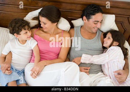 Family relaxing on bed in bedroom smiling (selective focus) Stock Photo