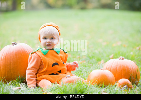 Baby boy outdoors in pumpkin costume with real pumpkins Stock Photo