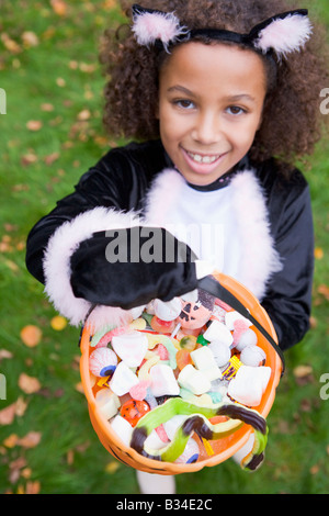 Young girl outdoors in cat costume on Halloween holding candy Stock Photo