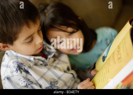 Boy aged six reads a story to his little sister aged five Stock Photo