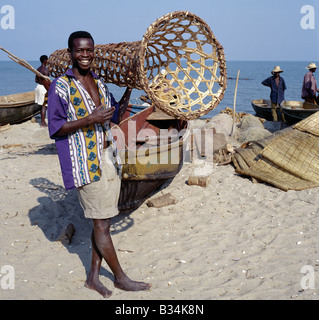 Uganda, Lake Edward, Rwenshama. A young man carries a wicker fish trap, which is used to catch fish in river estuaries. Rwenshama is an important fishing village on the shores of Lake Edward, close to the Queen Elizabeth National Park. Hippos can be just seen wallowing just offshore.Lake Edward, 2,995 feet above sea level, lies on the floor of the western branch of Africa's Great Rift Valley system and is connected to Lake George by the Kazinga Channel. Stock Photo