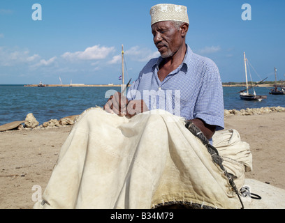 Kenya. A fisherman repairs the sail of his wooden sailing boat, known as mashua, along the waterfront of Kisingitini, a natural Stock Photo