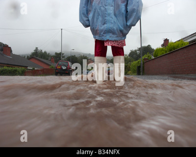 young girl wearing raincoat and wellington boots standing in water from rain and river overflow flooding a street  newtownabbey Stock Photo