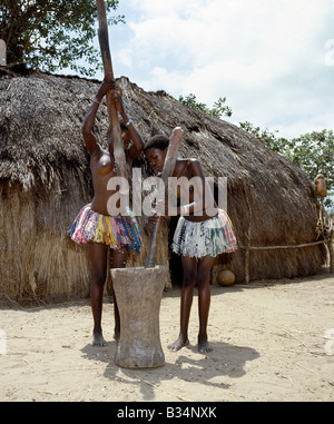 Kenya, Malindi, Gongoni. Two Giriama girls pound corn outside their home using a large wooden mortar and pestles. Stock Photo