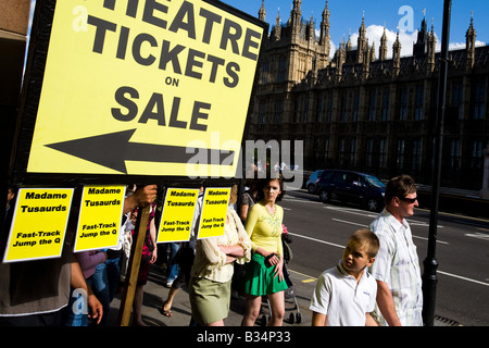 Pedestrians walk by a man holding a large sign advertising theatre tickets for sale in London, UK Stock Photo