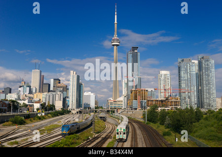 GO and VIA trains leaving downtown Toronto Union Station after work with highrise towers and CN Tower Stock Photo