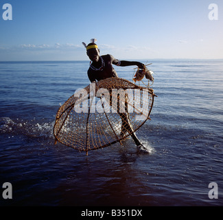Kenya, Lake Turkana, Eliye. With his traditional fishing basket poised, a Turkana fisherman rushes to catch a tilapia. Stock Photo