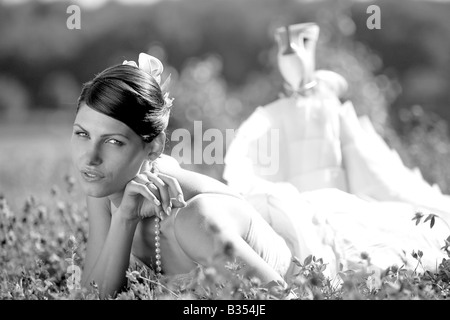 Portrait of beautiful bride in white dress lying down in field. Stock Photo