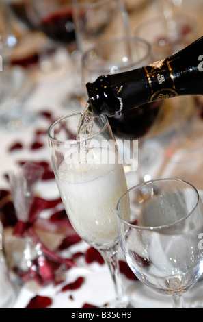 Champagne being poured in to a glass at a wedding reception in the UK.  There are red rose petals on the table. Stock Photo