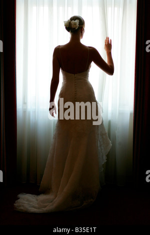 Beautiful bride seen in traditional wedding dress in silhouette at window. Stock Photo