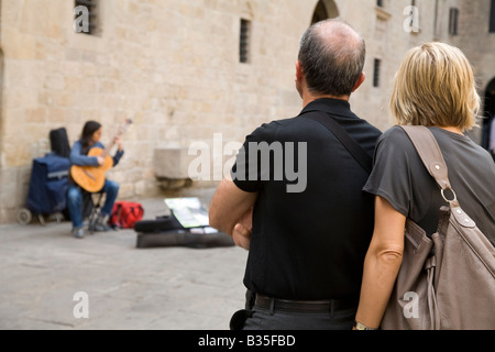 SPAIN Barcelona Middle age tourist couple watch female acoustic guitar playing in Placa del Rei plaza King s Square Stock Photo