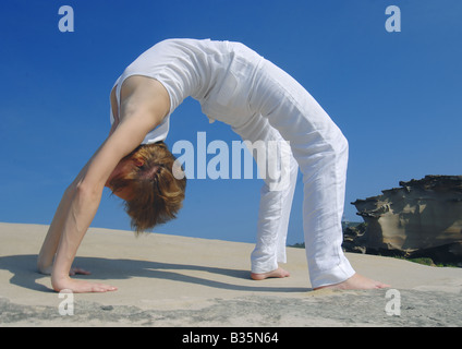 Nude woman bending backwards on rock with hands together Stock Photo